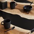 Minimalist composition on the design wooden and epoxy table with black teapot, cups and spoon. Modern dining room interior.