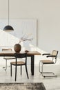 Minimalist composition of dining room interior with wooden table, design chairs, dried flowers in a vase, black pendant lamp, art. Royalty Free Stock Photo
