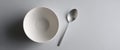 Minimalist composition of empty white bowl and stainless steel spoon on light gray surface with soft shadow Royalty Free Stock Photo