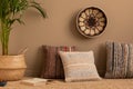 Minimalist composition of ethno living room interior with patterned, colorful pillows, brown wall, braided carpet, round basket on