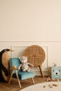 Minimalist composition of kid room interior with blue armchair, plush toys, wooden blocks, rattan sideboard, beige wall with