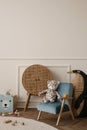 Minimalist composition of kid room interior with blue armchair, plush toys, wooden blocks, rattan sideboard, beige wall with