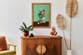 Minimalist composition of living room with brown mock up picture frame, plant, retro armchair, dried tropical leaf, decoration. Royalty Free Stock Photo