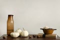 Minimalist composition of living room interior with wooden commode, pumpkins, brown glass carafe, bowl with nuts, books, beige