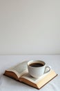 A minimalist depiction of an open book and a cup of coffee on a white background