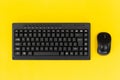 Minimalist flat lay of black wireless keyboard and mouse on a vibrant yellow background Royalty Free Stock Photo