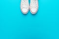Minimalist flat lay image of white gumshoes over turquoise blue background