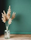 Minimalist glass vase of dried grasses on a green background.