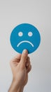 Minimalist Hand Holding Blue Sad Emoji Circle on White Background Royalty Free Stock Photo