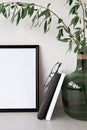 Minimalist home office workspace, blank picture frame mockup, books, glasses and green vase with plants. Aesthetic neutral house