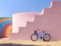 Minimalist image of a blue bicycle leaning against a pink staircase with a rainbow colored heel, made with generative ai