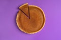 Minimalist image of a pumpkin pie, with one sliced piece and separated, on a purple background. Top view. Traditional dessert.