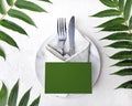 Minimalist mock wedding or  birthday table setting with silver cutlery, marble plate, vintage napkin and tropical leaves on white Royalty Free Stock Photo