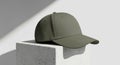 Minimalist Olive Green Baseball Cap on a White Pedestal with Shadow Play Royalty Free Stock Photo