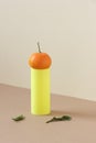 Minimalist still life with citrus fruit on bright cylinder geometric shape with leaves on the side on beige table background