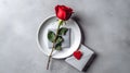 Minimalist Valentine\'s Day setup with a single rose and envelope on a flat gray surface