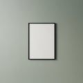 A minimalist vertical blank poster with a black frame hangs on a light gray wall. The Royalty Free Stock Photo