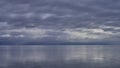 View over the calm ocean of an approaching rain storm with cloud reflections.