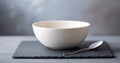 Minimalist white ceramic bowl with a silver spoon placed on a dark slate serving board against a soft blurred background Royalty Free Stock Photo