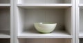 Minimalist white shelving unit with a single light green ceramic bowl centered on a middle shelf in a modern interior setting Royalty Free Stock Photo