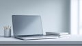 Minimalist workspace with closed laptop, stack of notebooks, and pencil holder on clean white desk against soft gray background Royalty Free Stock Photo