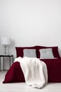 A minimalistic bedroom interior with a bed dressed in burgundy linen, gray quilted cushions and vanilla soft blanket. White copy s Royalty Free Stock Photo