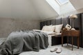 Minimalistic bedroom interior with grey bed, beige bedclothes, wooden night table and elegant personal accessories. Roof window. Royalty Free Stock Photo