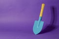 Minimalistic composition with a blue garden shovel on a lilac ba