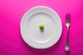 A minimalistic composition showcases a single green pea resting gracefully on a white plate, accentuated by a bold pink Royalty Free Stock Photo