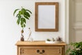Minimalistic compositon with wooden vintage commode, brown mock up photo frame, avocado plant, plants and personal accessories.