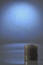 Single extinguished candle with rising smoke on reflective surface and blue background symbolizing silence memory and peace Royalty Free Stock Photo