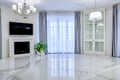 Minimalistic interior of living room in light tone with marble flooring, large windows and fireplace under TV