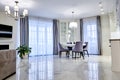 Minimalistic interior of living room in light tone with marble flooring, large windows and a table for four persons