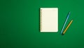 Minimalistic simple workspace design with notepad, pen and pencil, green background, top view, copy space banner