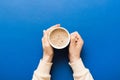 Minimalistic style woman hand holding a cup of coffee on Colored background. Flat lay, top view cappuccino cup. Empty Royalty Free Stock Photo
