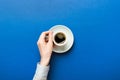 Minimalistic style woman hand holding a cup of coffee on Colored background. Flat lay, top view cappuccino cup. Empty Royalty Free Stock Photo