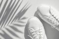 Minimalistic summer background with shoes. White women's leather sneakers, sun shade from tropical leaf on white Royalty Free Stock Photo