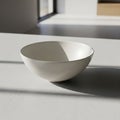 Minimalistic white ceramic bowl sits on a smooth surface in a brightly lit Royalty Free Stock Photo