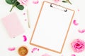 Minimalistic workspace with clipboard, pink roses, notebook and pen on white background. Flat lay, top view.