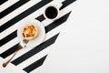 Minimalistic workspace with cup of coffee, bakery, isolated on striped black and white background. Flat lay style Top view. Royalty Free Stock Photo