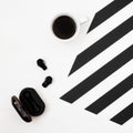 Minimalistic workspace with cup of coffee, wireless earphones on striped black and white background. Flat lay style Top view. Royalty Free Stock Photo