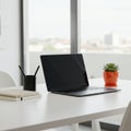 Minimalistic workspace featuring a sleek laptop on a white table. Beside it, a red pot Royalty Free Stock Photo