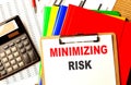 MINIMIZING RISK text on clipboard with calculator and color folder