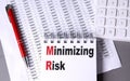 MINIMIZING RISK text on notebook with pen, calculator and chart on grey background