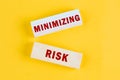MINIMIZING RISK text on wooden blocks on a light mustard background. View from above