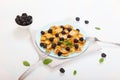 Minipancakes with blackberries lie on a blue plate, next to two forks on a white background