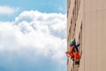 Industrial climber washes windows on facade of a building. Side view with sky and clouds Royalty Free Stock Photo