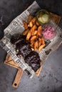 Minsk, Belarus - August, 2019 Top view on BBQ Pork ribs set with baked potato and pickled cucumber serve with newspaper on wooden