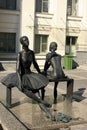 A very beautiful statue of two ballerinas dressed in tutu skirts sitting on a bench on the street