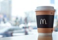 Minsk, Belarus, February 18, 2018: Paper cup of coffee with McDonald`s logo on table near window on background of blurred city in